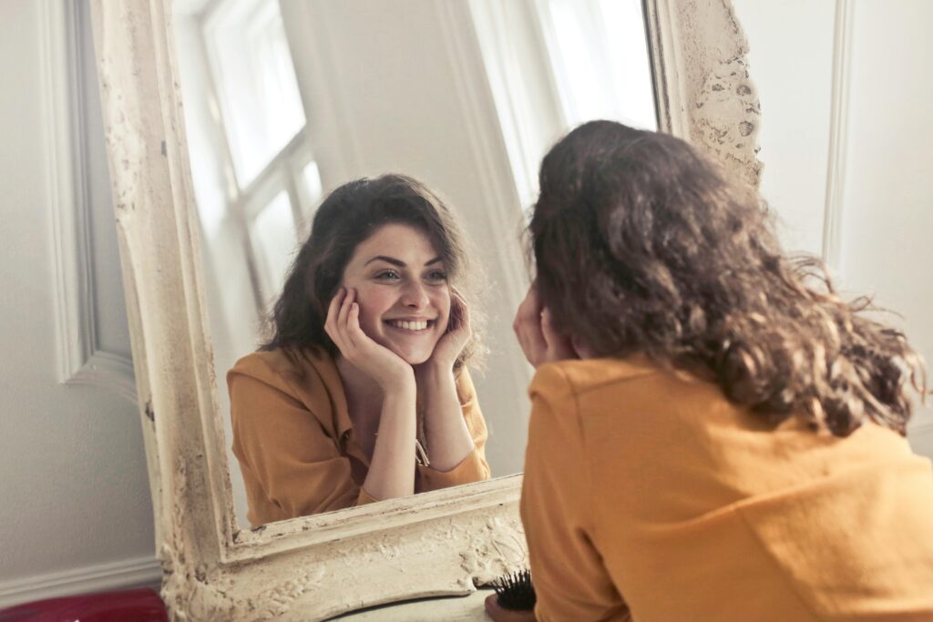 다이어트 정체기 탈출법|적게 먹는데 살이 안 빠지는 진짜 이유와 대사 회복 전략 A cheerful woman smiles at her reflection in a vintage-style mirror, exuding positivity and warmth.
