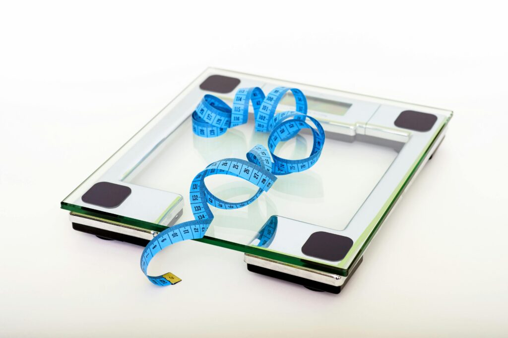 다이어트 정체기 탈출법|적게 먹는데 살이 안 빠지는 진짜 이유와 대사 회복 전략 A digital glass weighing scale with a blue measuring tape, symbolizing weight management.