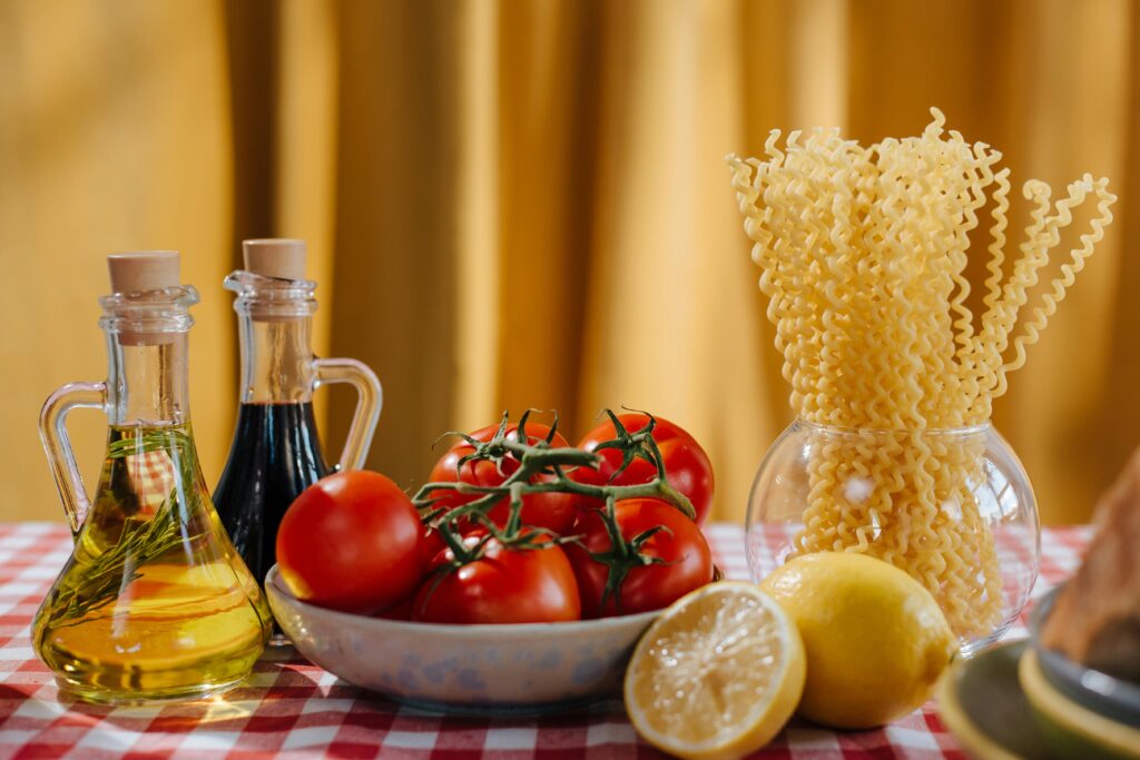 ํ์คํ๐ ๋ค์ด์ดํธ, 40๋๋ ์ด ์์ฐ๊ฒ ๋จน๋ ๋ฐฉ๋ฒ! Vibrant still life of Italian cooking ingredients including tomatoes, pasta, and olive oil on a checkered tablecloth.